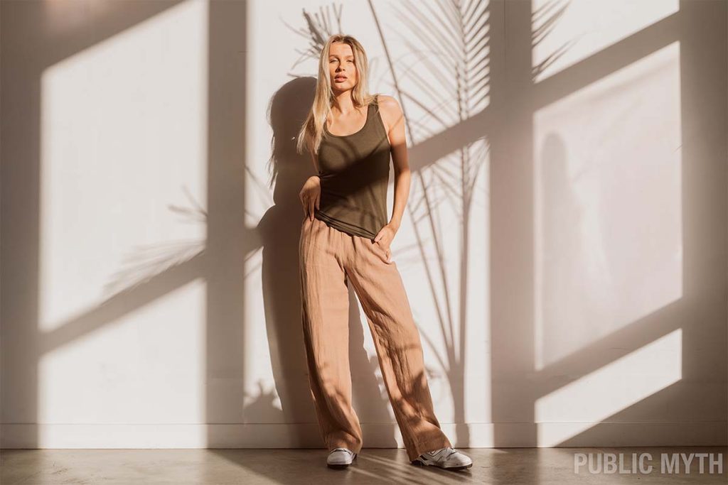 A blonde women wearing beige linen pants with an olive green tank top outfit 