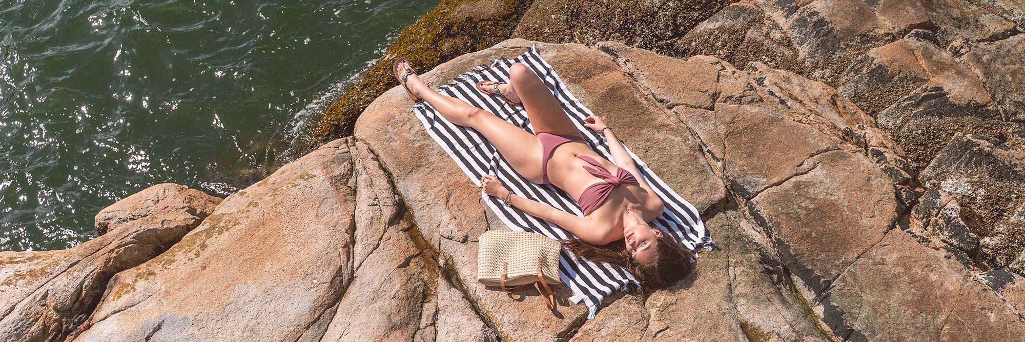 A woman wearing a Tencel Lyocel organic bikini laying oceanside on a flat rock on a warm sunny day.